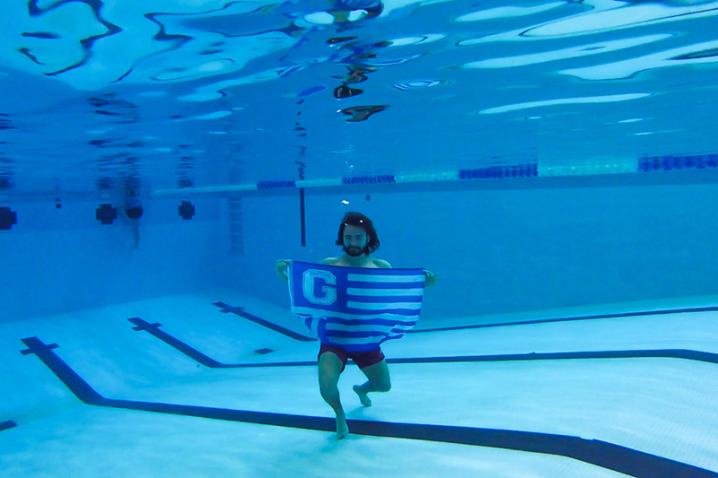 Student under water in a swimming pool holding a 香妃直播 Flag